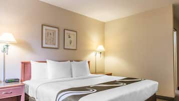 A hotel room with a bed, two bedside lamps, a nightstand, a framed picture, and a wall-mounted lamp.