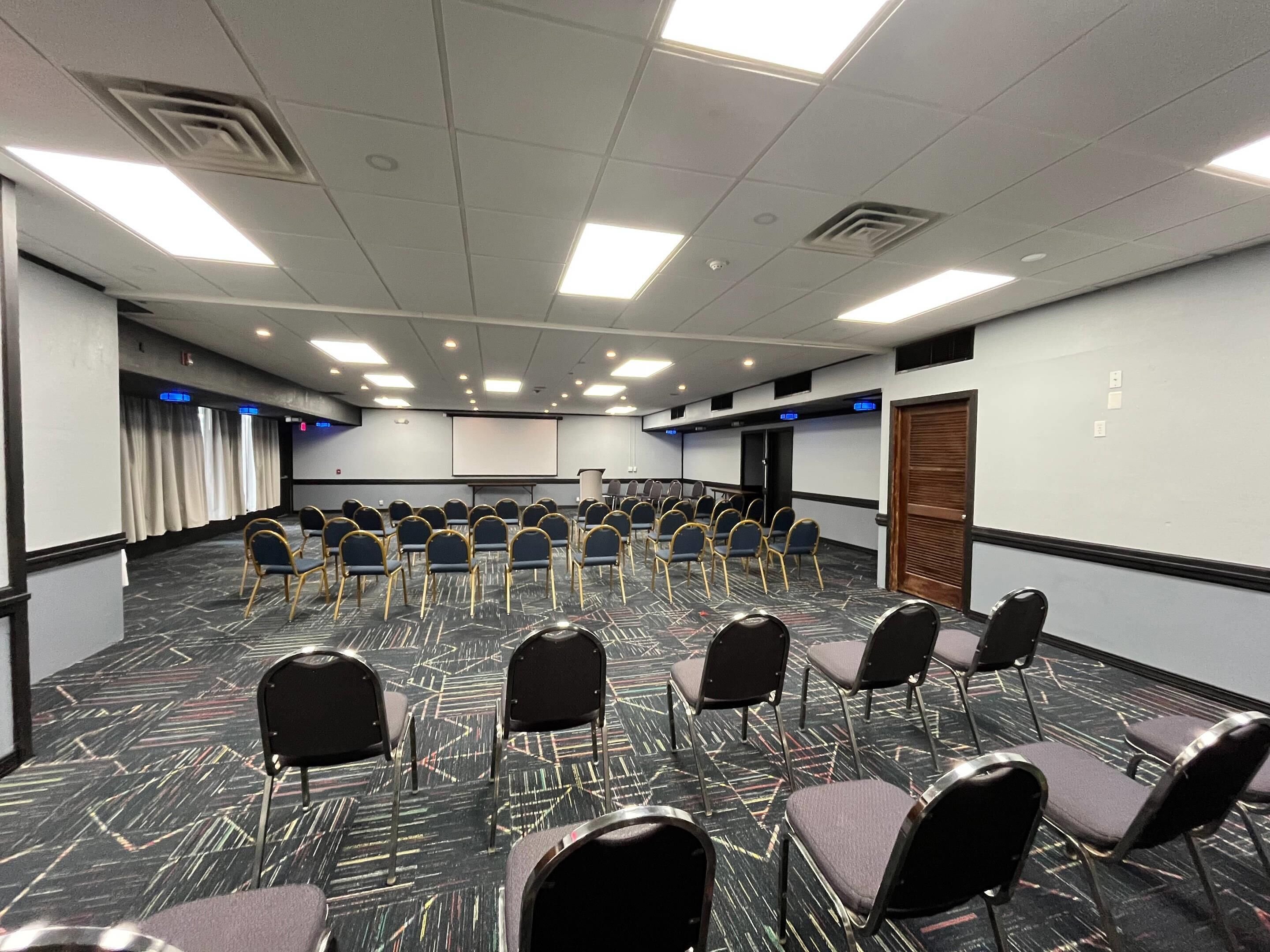 A conference room with rows of chairs, a projector screen, and a carpeted floor.