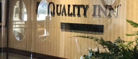 A reception area with a 'QUALITY INN' sign, a reception desk, and a potted plant.