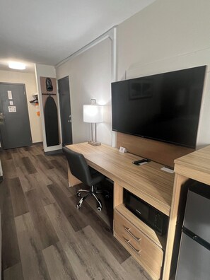 A hotel room with a wooden desk, a flat-screen TV, a lamp, a microwave, and a refrigerator. - Quality Inn Hermitage South (Hermitage)