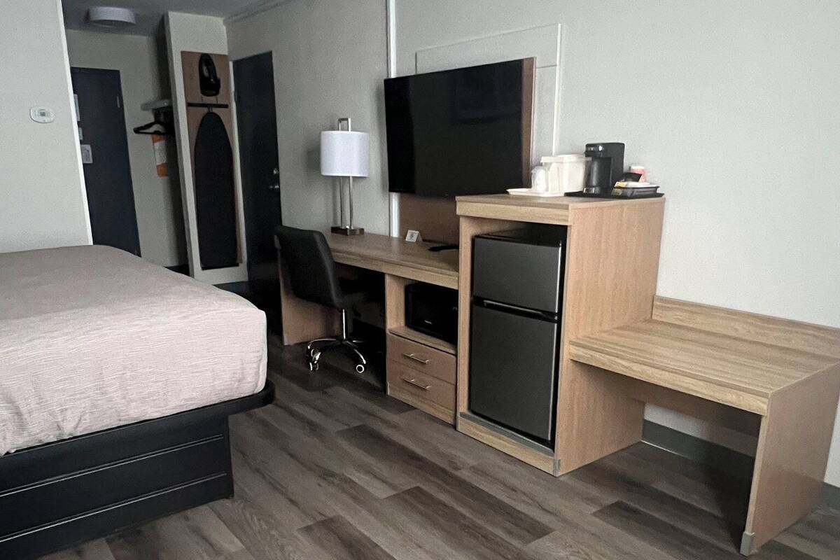 A hotel room with a bed, desk, TV, refrigerator, and a small kitchenette.