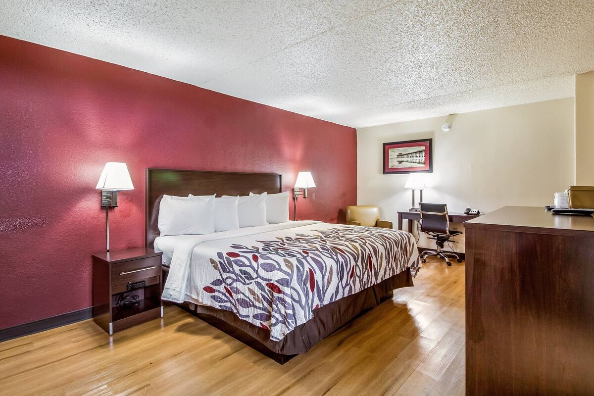 A hotel room with a bed, bedside tables, a desk, and a chair.
