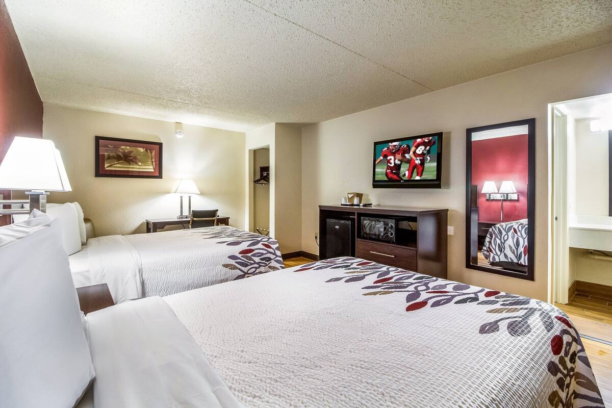 A hotel room with two beds, a TV, a desk, and a mirror.