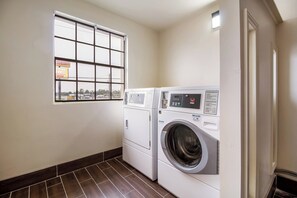 A laundry room with two front-loading washing machines, a window with a view of the outside, and a tiled floor.