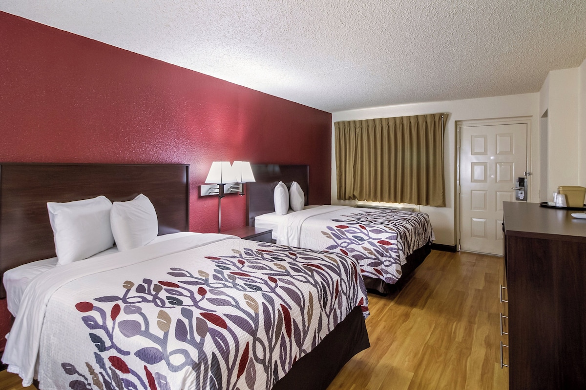 A hotel room with two beds, a desk, a lamp, and a door.