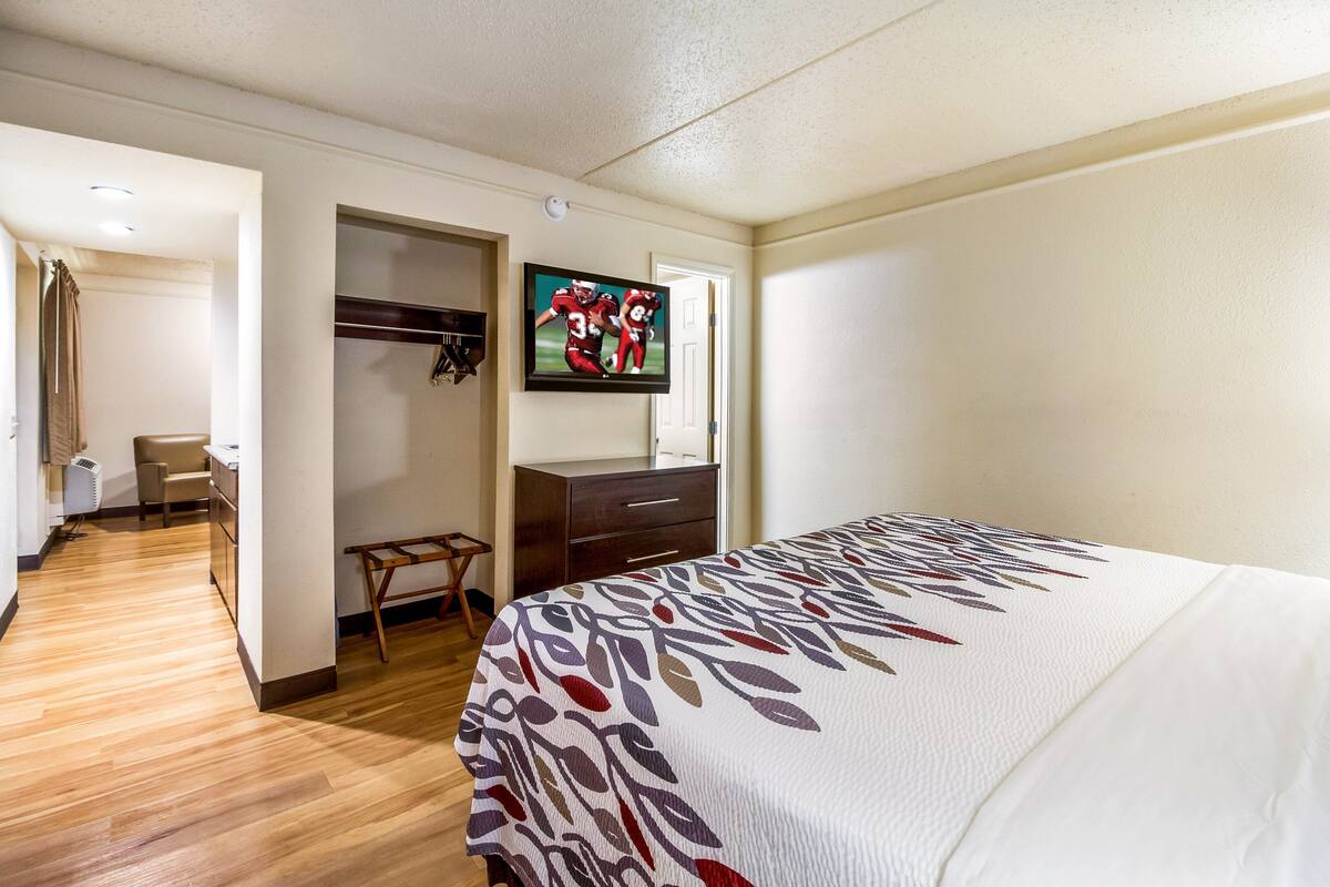 A hotel room with a bed, a desk, a chair, a wardrobe, and a television on the wall.