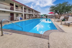 A swimming pool with a diving board, lounge chairs, and a fenced area with tables and umbrellas. - Red Roof Inn Houston East – I-10 (Houston)