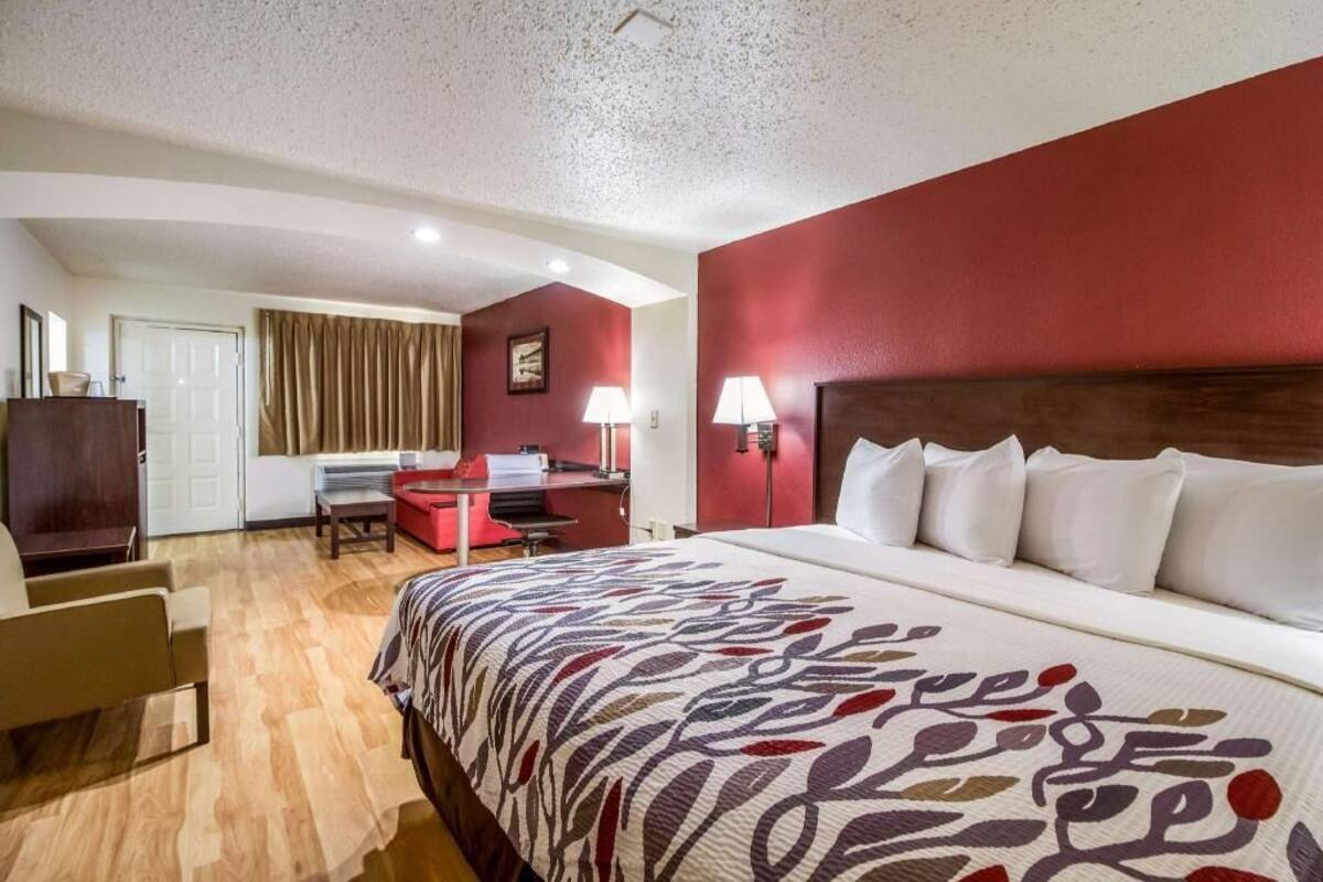 A hotel room with a bed, desk, chair, and a view of the outside.
