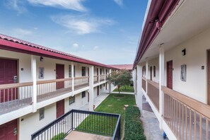 A corridor with multiple balconies, a central lawn area, and a clear sky. - Red Roof Inn Houston East – I-10 (Houston)