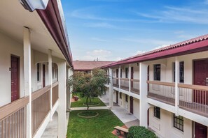 A courtyard with a central tree, surrounded by buildings with balconies and red-tiled roofs. - Red Roof Inn Houston East – I-10 (Houston)