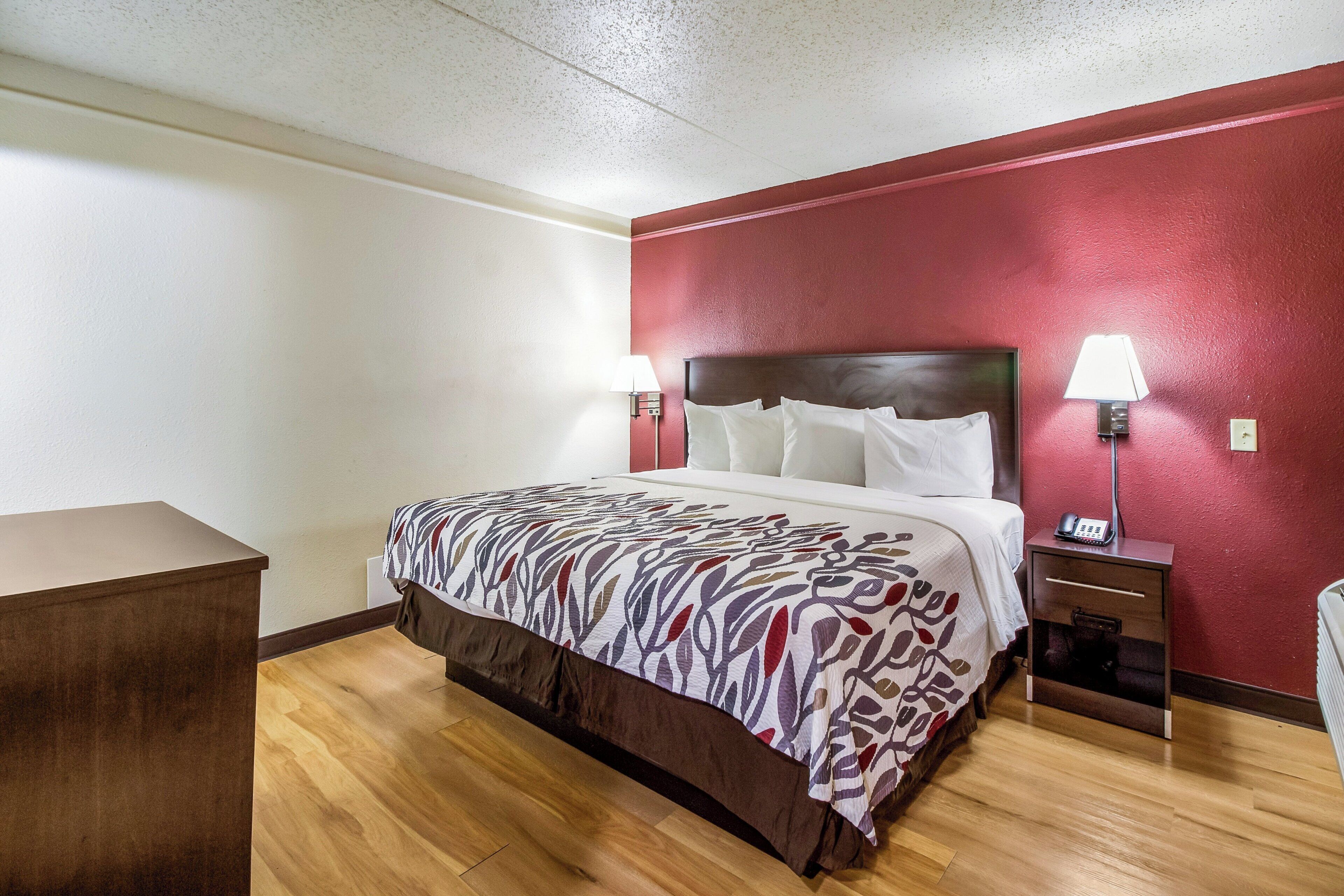 A hotel room with a bed, bedside lamps, a wooden nightstand, and a desk.