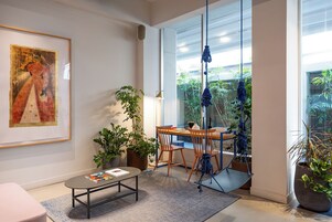 A modern living room with a large window, a painting on the wall, and a dining area with a table and chairs.