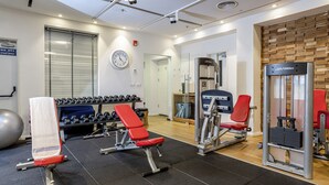 Ein Fitnessraum mit Trainingsgeräten, einer Uhr und einem Fenster mit Jalousien.