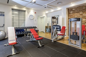 Ein Fitnessraum mit Trainingsgeräten, einer Uhr und einem Fenster mit Jalousien.
