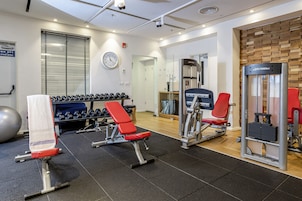 Un gimnasio con equipo de ejercicio, un reloj y una ventana con persianas.