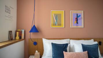 A hotel room with a bed, pillows, a bedside table, a lamp, and two framed artworks on the wall.