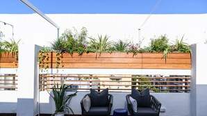 Een terras op het dak met twee rieten stoelen, een potplant en een houten plantenbak met diverse planten.