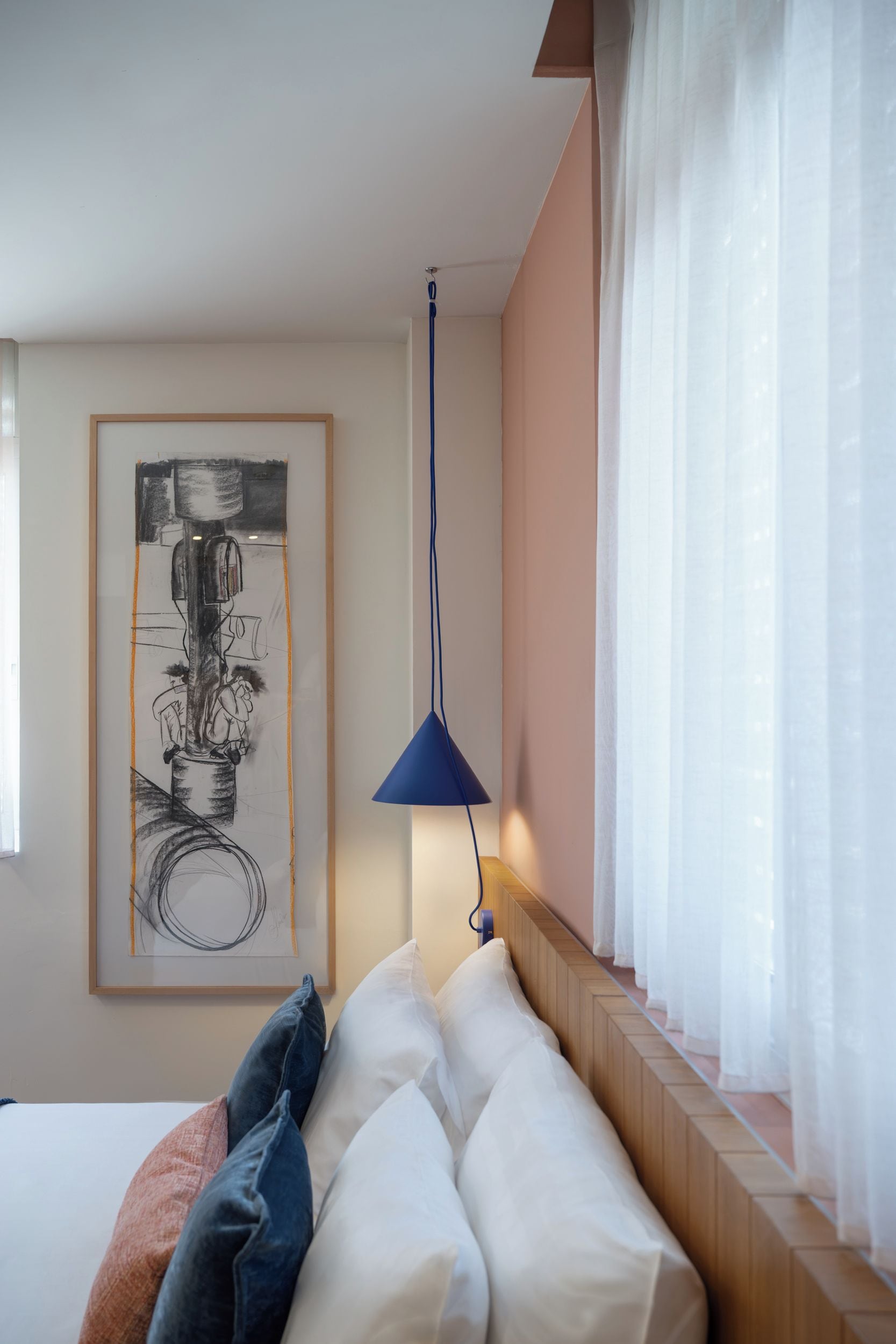 Habitación de hotel con cama, una obra de arte enmarcada, una lámpara colgante azul y cortinas traslúcidas.