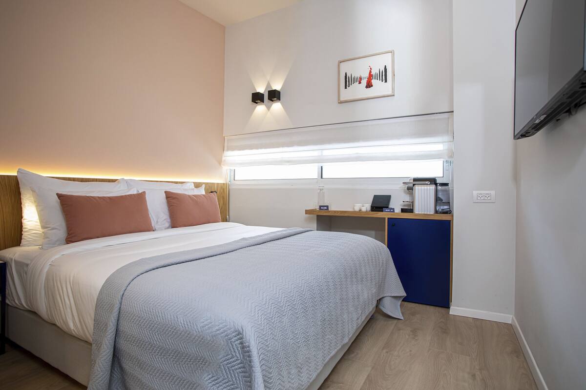 Une chambre d’hôtel comprenant un lit, une table de chevet, une lampe et un petit bureau avec une chaise.
