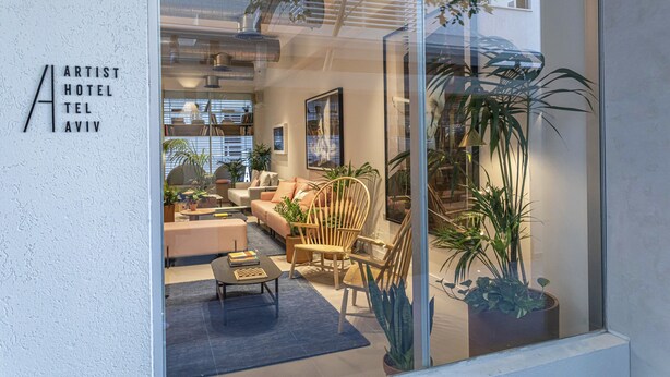 Een moderne hotellobby met een zithoek, potplanten en een glazen wand.