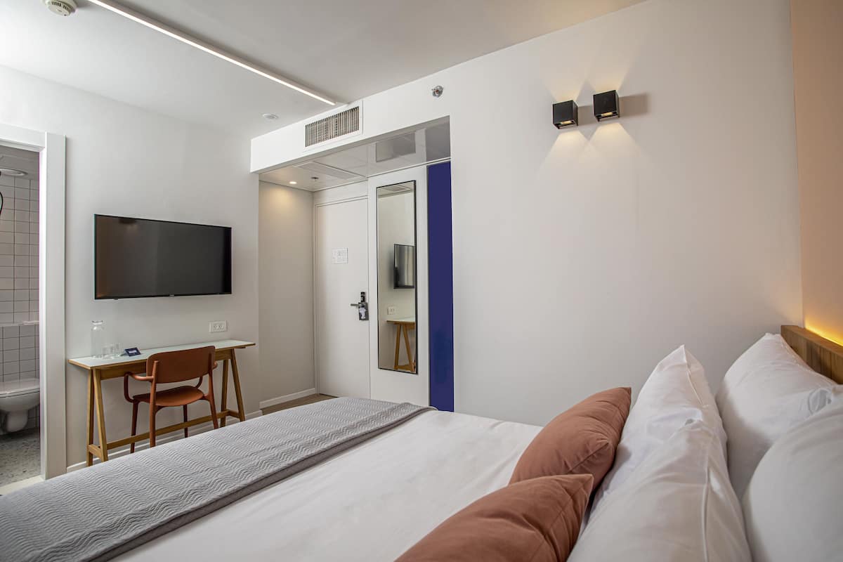 Une chambre d’hôtel moderne équipée d’un lit, d’un bureau, d’une chaise, d’une télévision et d’un miroir.