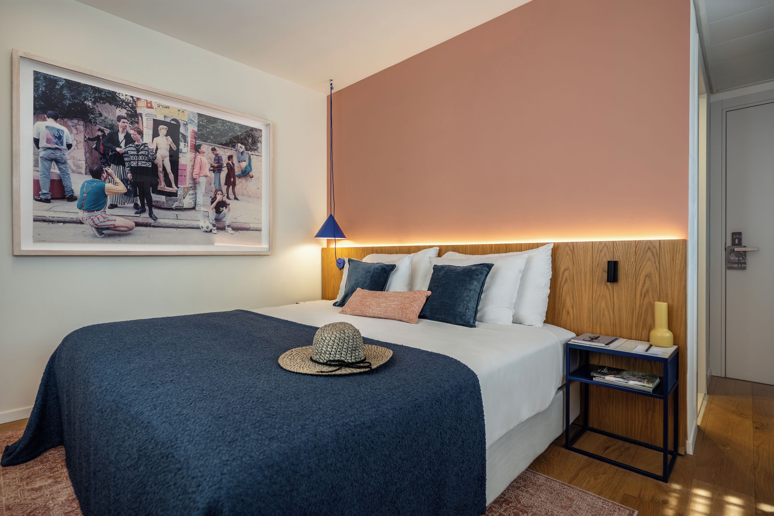 Un dormitorio con cama, mesita de noche, lámpara, estante en la pared y un cuadro enmarcado.