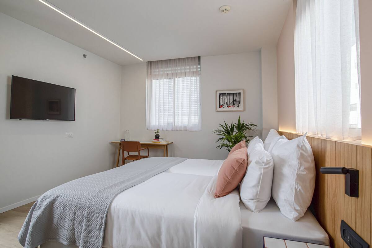 Une chambre moderne avec un lit, une table de chevet, une télévision et une fenêtre avec des rideaux.