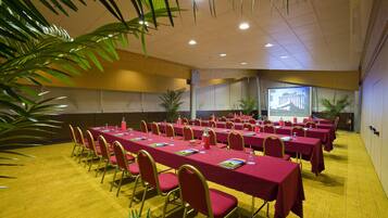 Une salle de conférence avec de longues tables, des chaises rouges et un écran de projection.