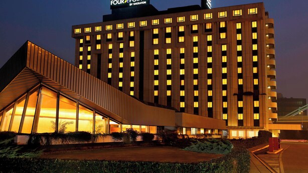 Et hotel med moderne design, med et markant 'Four Points by Sheraton' skilt, en stor glasfacade og en unik, vinkelformet tilbygning.