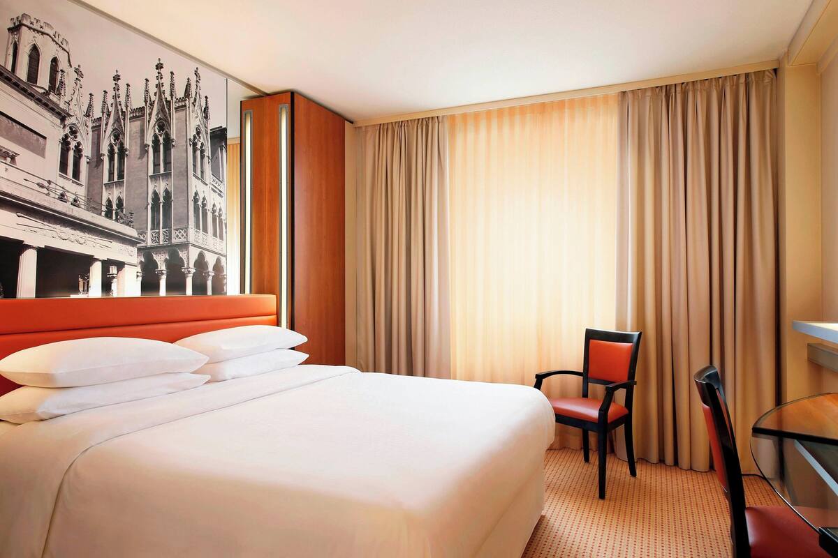 A hotel room with a large bed, a chair, a desk, and a wall mural.