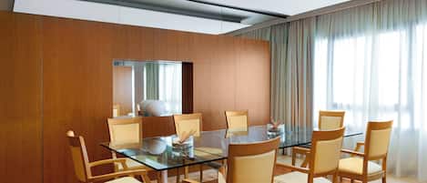 Un comedor moderno con una mesa de vidrio rodeada de sillas de madera, un espejo grande y vistas al exterior a través de amplias ventanas.
