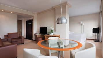 Ein modernes Hotelzimmer mit Glastisch, Ledersofas, einem Flachbildfernseher, einem Bett und einem großen Fenster.