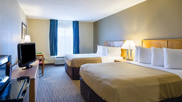 A hotel room with two beds, a desk with a television, and a window with curtains.