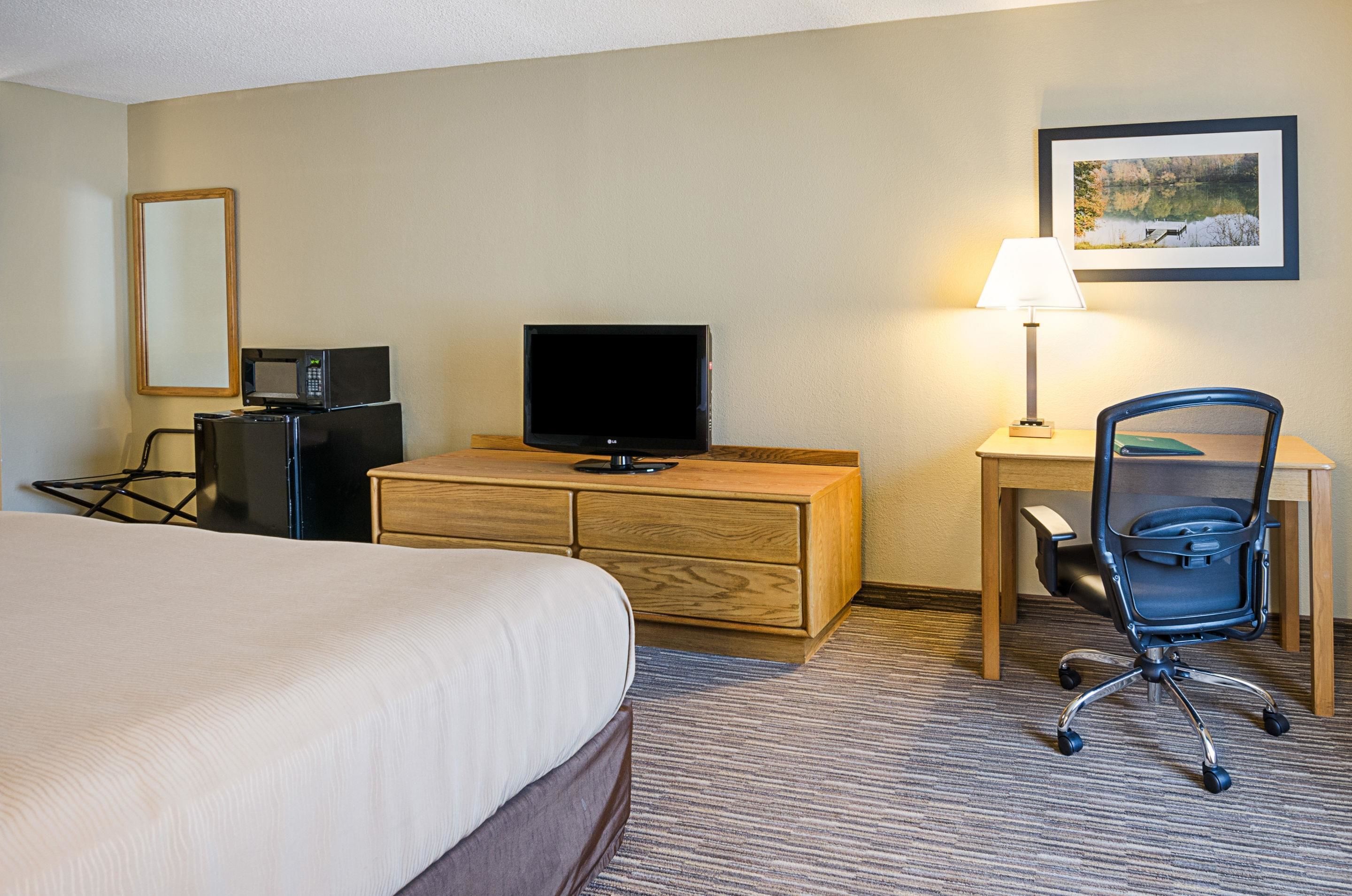 A hotel room with a bed, a desk with a lamp, a television, a chair, and a dresser.