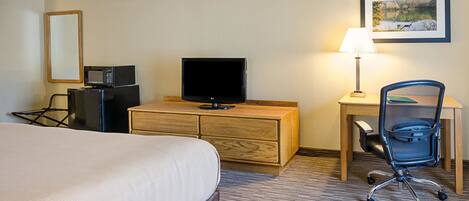 A hotel room with a bed, a desk with a lamp, a television, a chair, and a dresser.