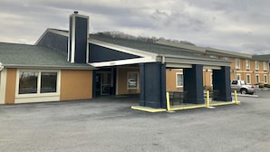 A hotel with a covered entrance, a parking lot, and a building with a chimney.
