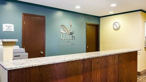 Un mostrador de recepción en Quality Inn con detalles de madera, un reloj en la pared y un letrero que indica que el hotel es 100% libre de humo.