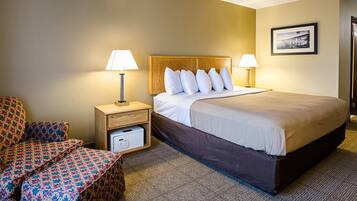 A hotel room with a large bed, two bedside lamps, a wooden nightstand, a patterned armchair, and a framed picture on the wall.