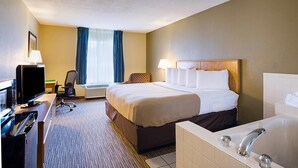 Habitación de hotel con cama, escritorio con computadora, silla, lámpara, equipo de aire acondicionado, ventana con cortinas y bañera.