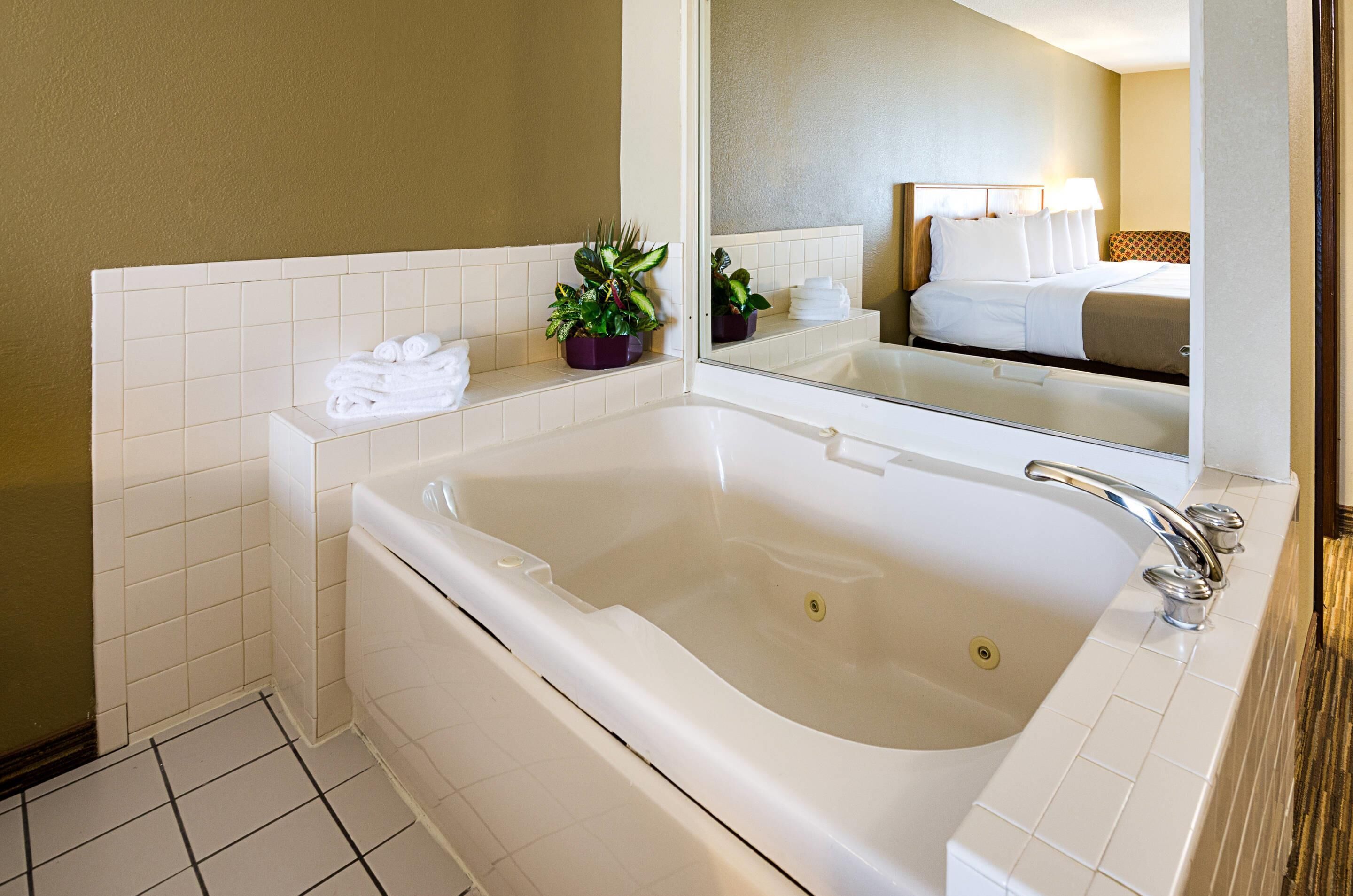 A modern bathroom with a large bathtub, a mirror, and a small potted plant.