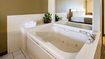 A modern bathroom with a large bathtub, a mirror, and a small potted plant.