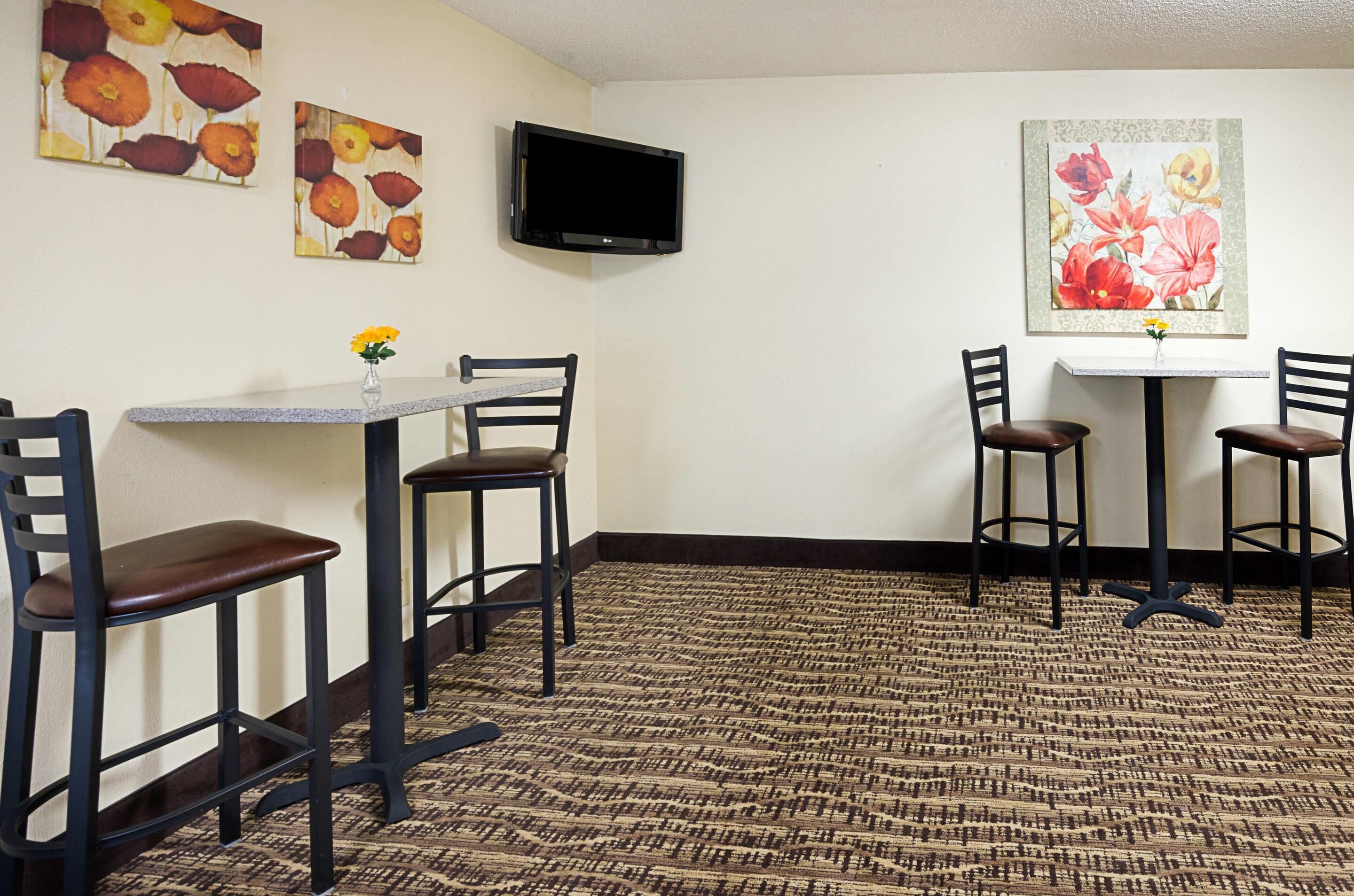Une chambre d’hôtel dotée d’un coin repas comprenant deux tables et quatre chaises, d’un téléviseur à écran plat fixé au mur et d’œuvres d’art florales décorant les murs.
