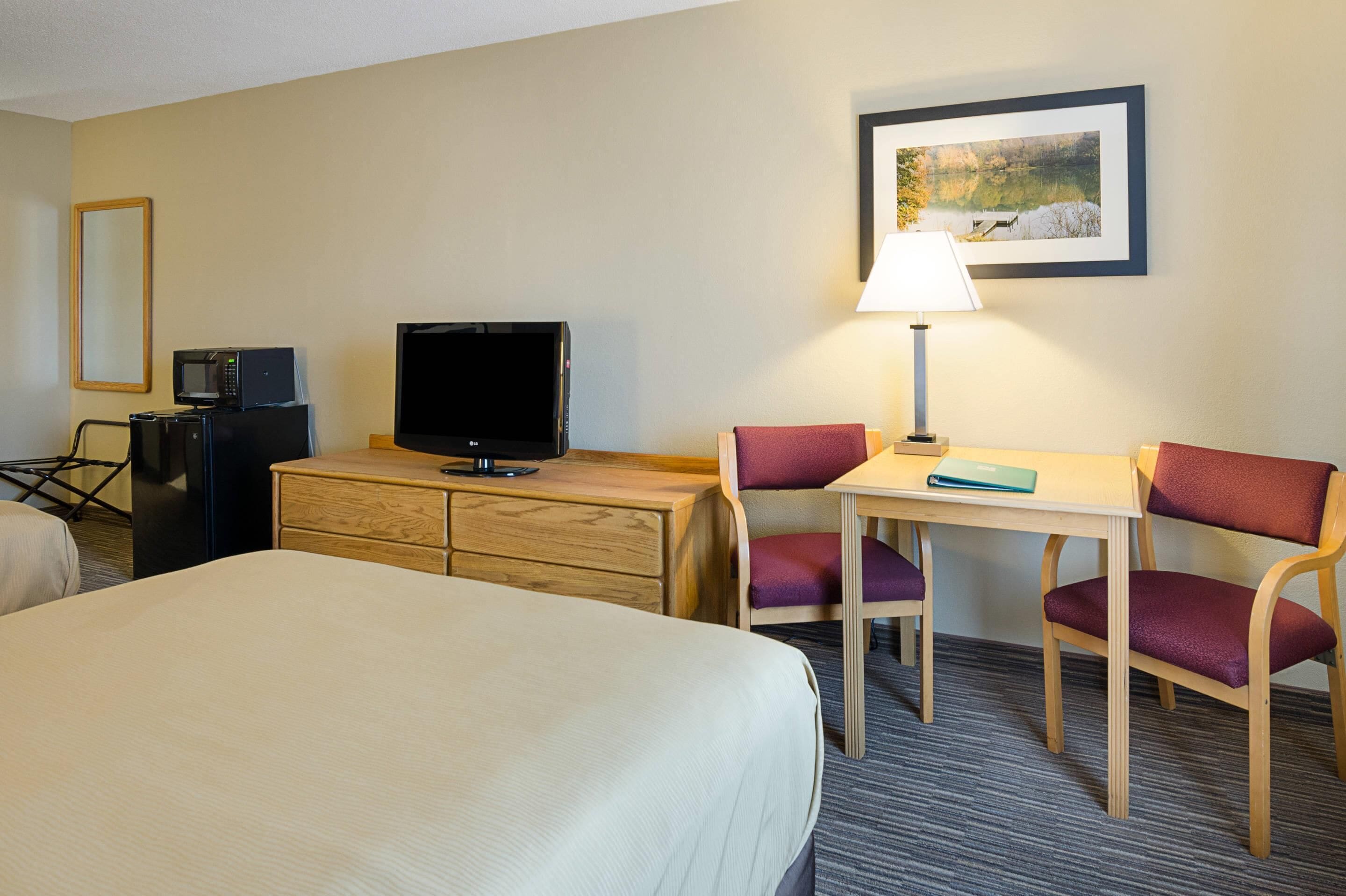 A hotel room with a bed, a desk with a lamp, a television, and a chair.