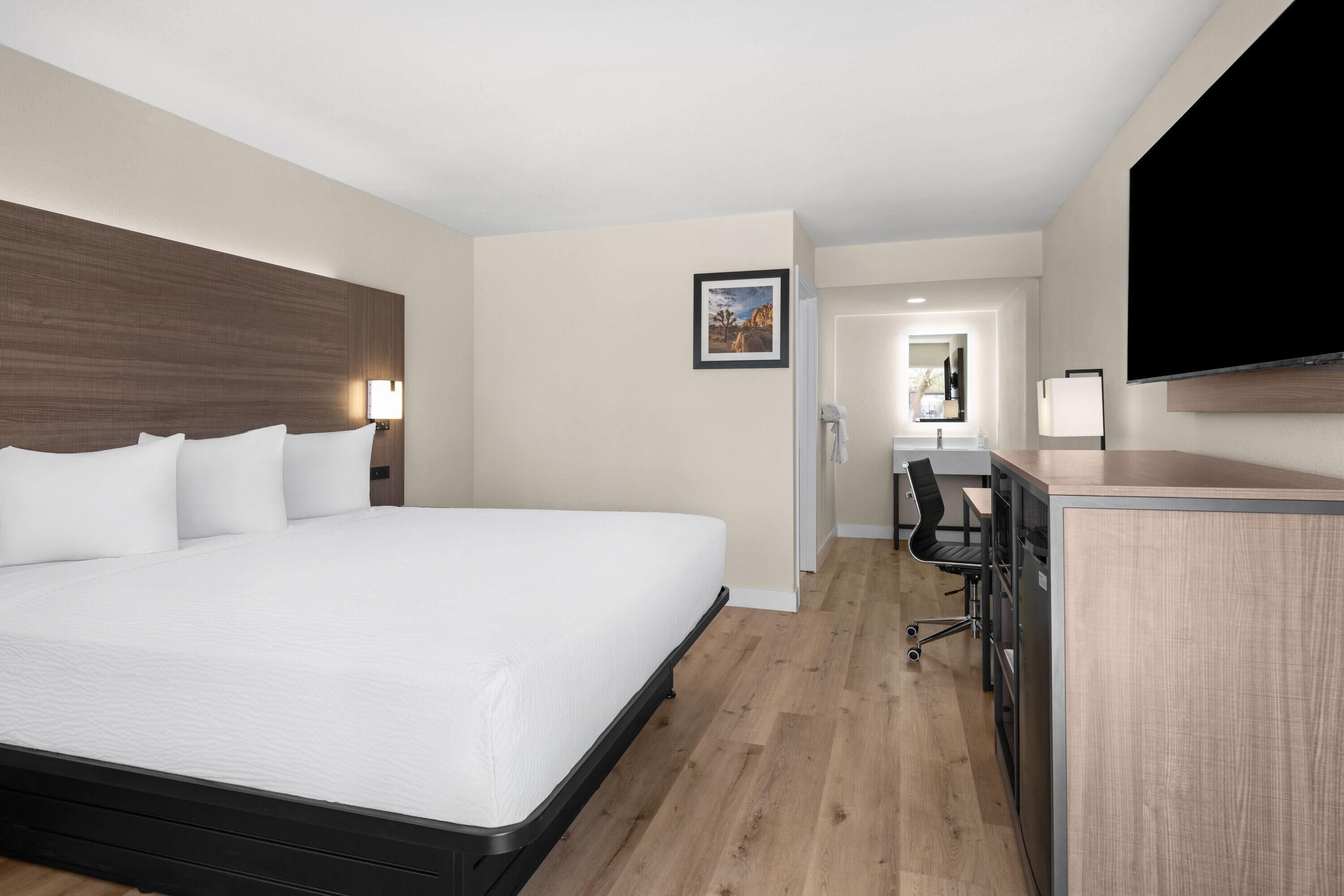 A hotel room with a large bed, a desk, a chair, a flat-screen TV, and a framed picture on the wall.
