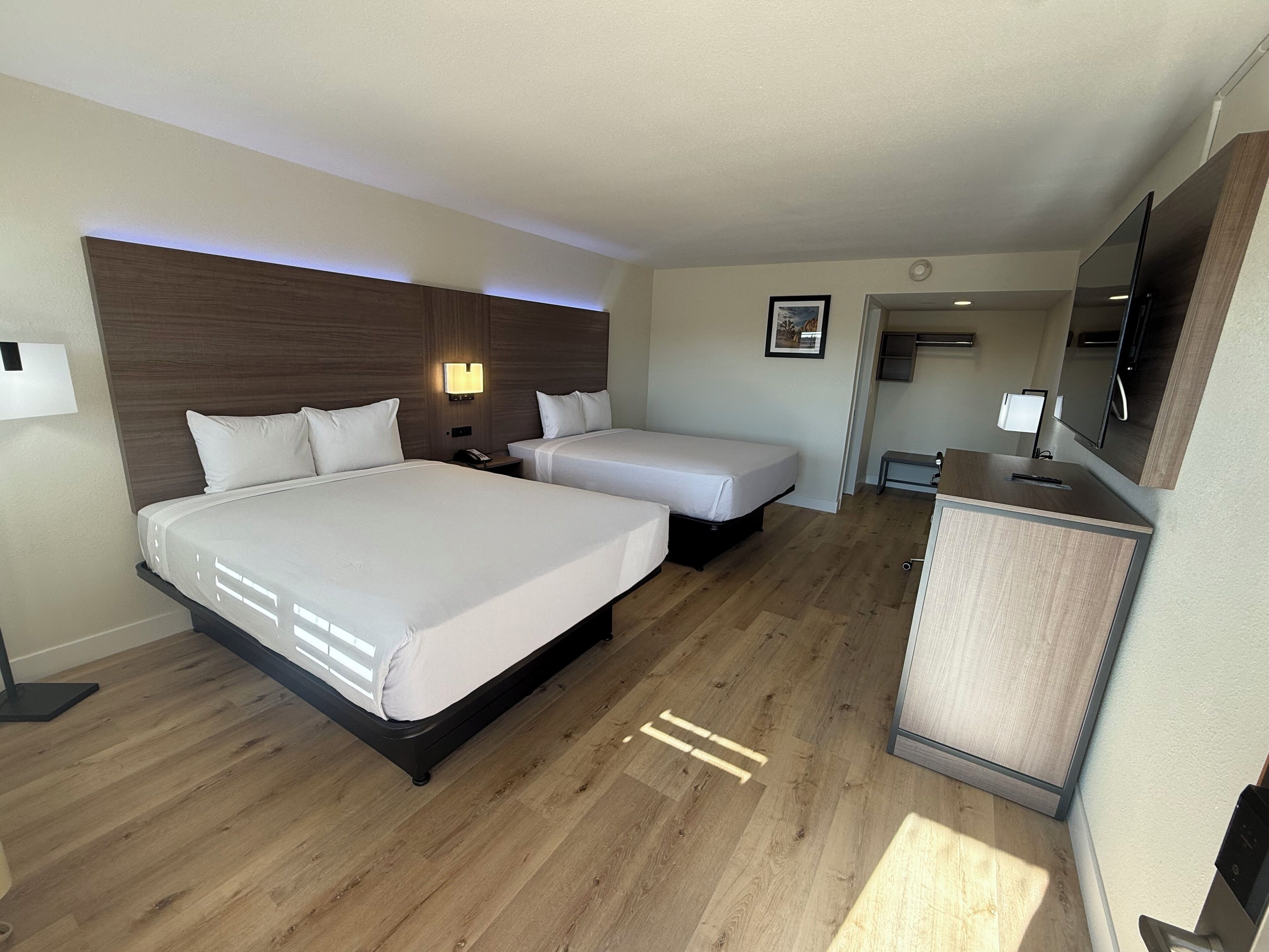 Ein Hotelzimmer mit zwei Betten, einem Schreibtisch, einem Spiegel und einer kleinen Sitzecke.