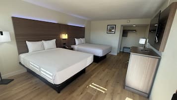 A hotel room with two beds, a desk, a mirror, and a small seating area.