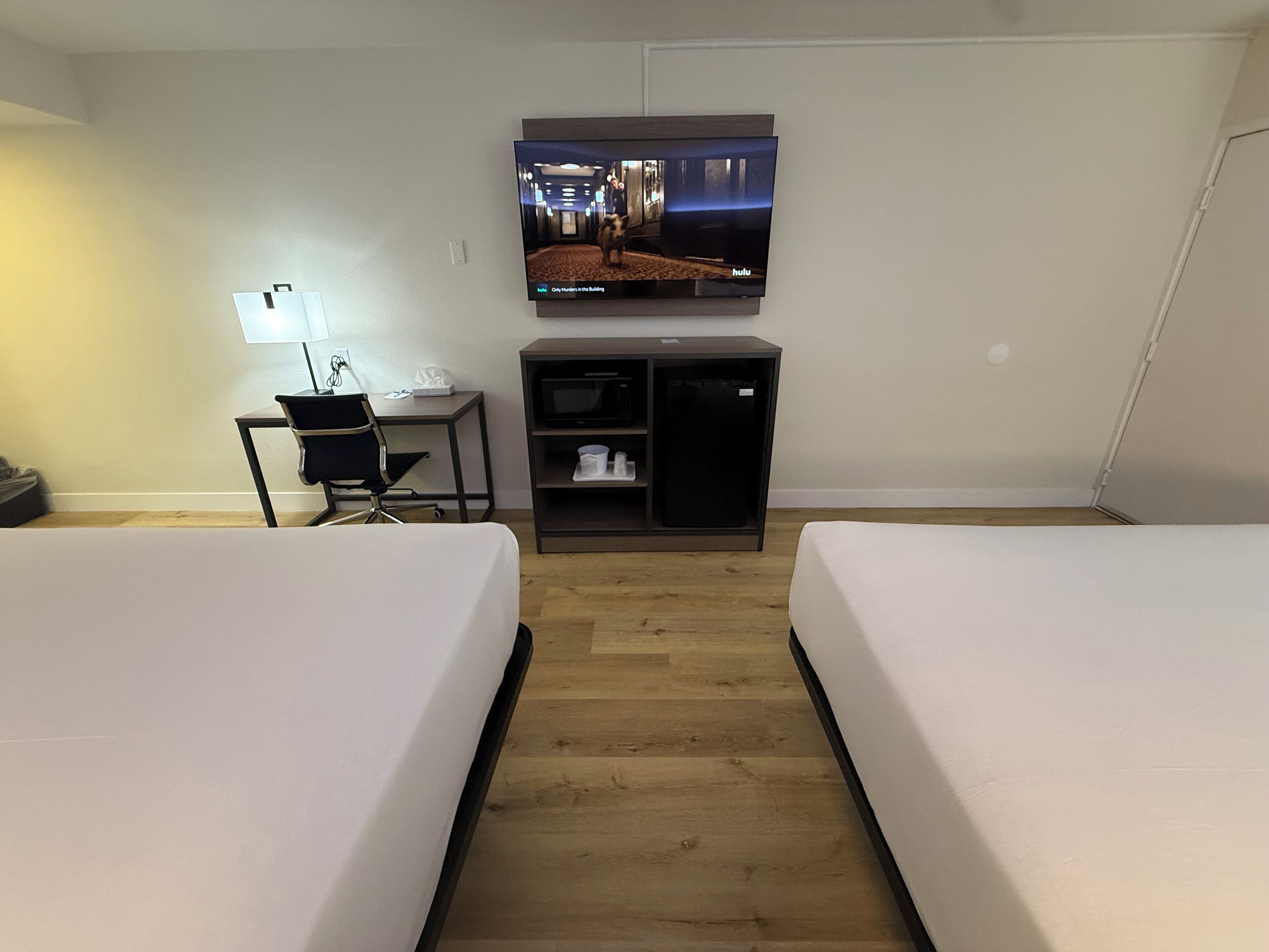 Habitación de hotel con dos camas, un escritorio, un televisor montado en la pared y un microondas en un mueble.