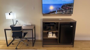 A hotel room with a desk, chair, lamp, flat-screen TV, and a minibar. - Travelodge by Wyndham Imperial/El Centro (Imperial)