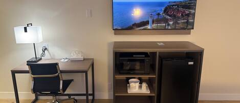 Habitación de hotel con escritorio, silla, lámpara, televisor de pantalla plana y minibar.