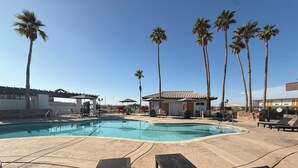 A pool area with lounge chairs, palm trees, and a small building with a tiled roof. - Travelodge by Wyndham Imperial/El Centro (Imperial)